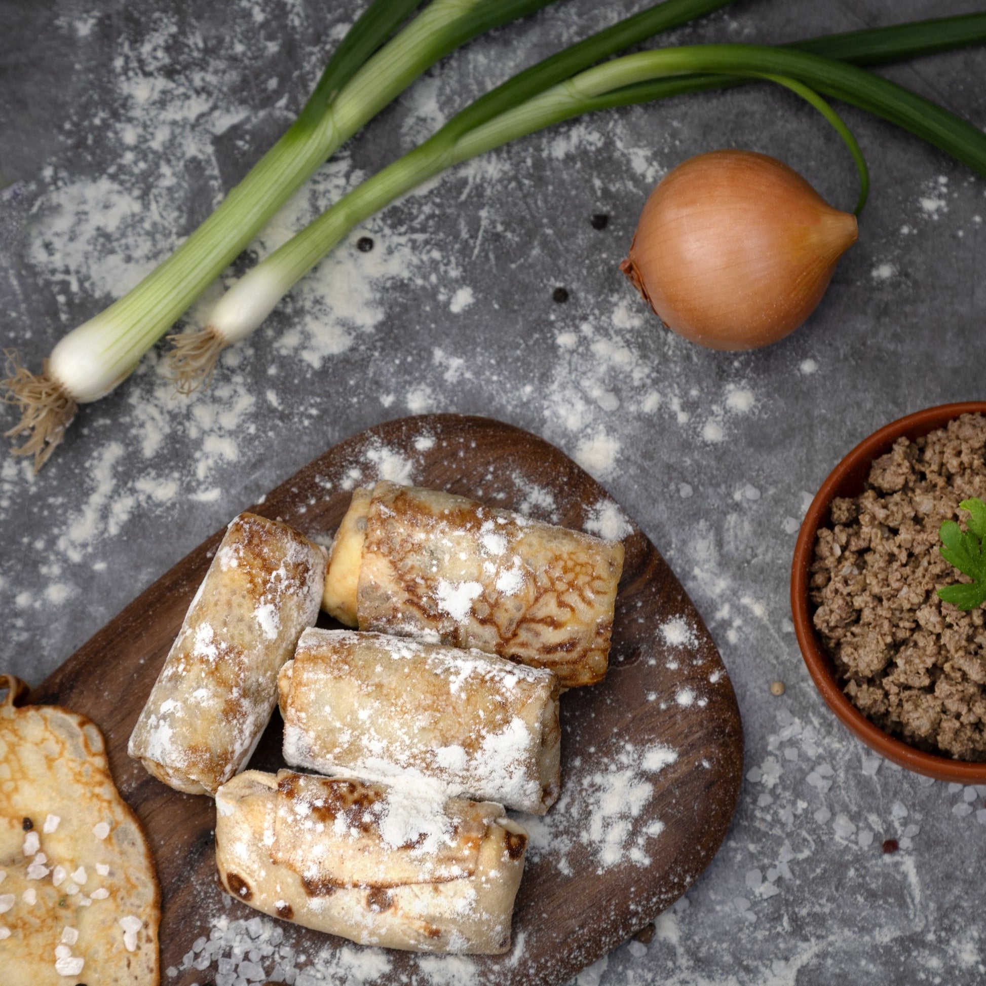 Raw beef and pork filled crepes on board with onions, flour, and minced meat—Eastern European prep scene.