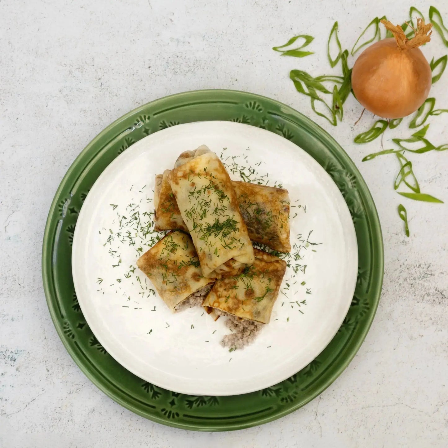 Top view of beef and pork stuffed crepes garnished with dill—traditional Slavic meat-stuffed blini.