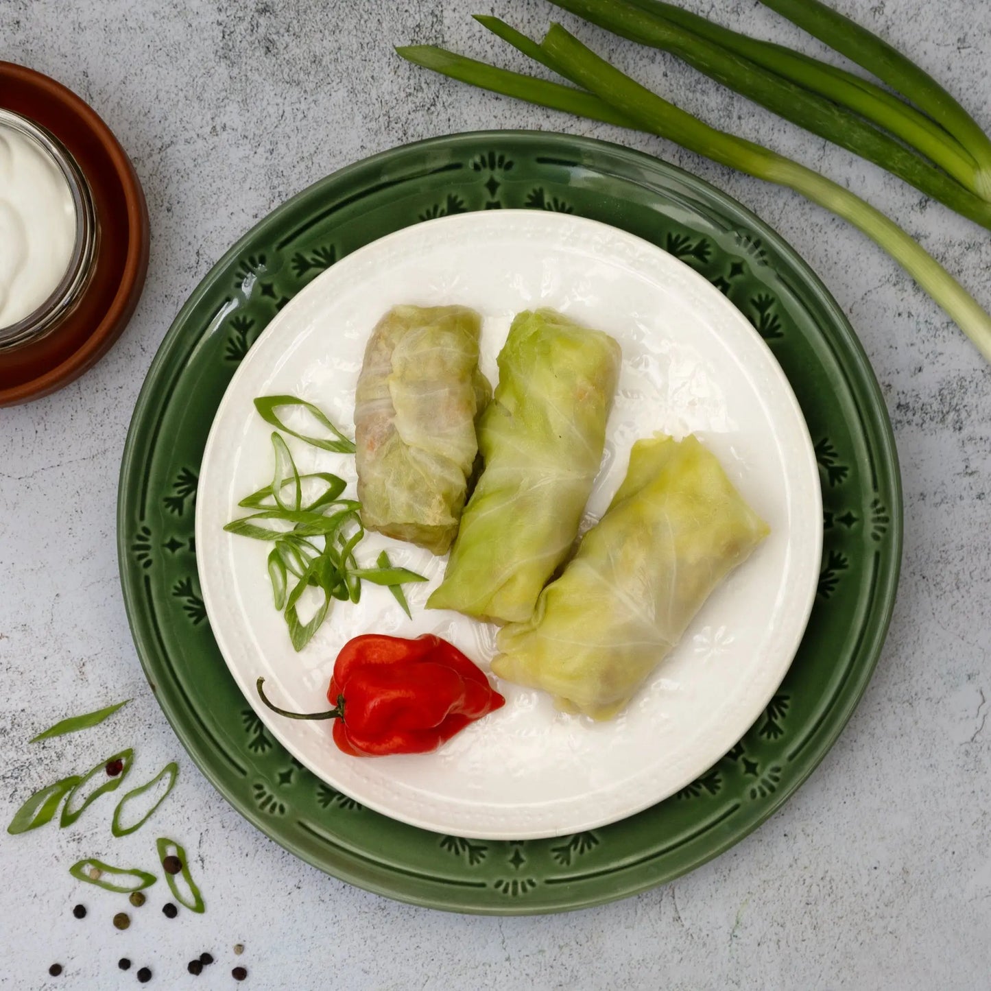 Top view of cooked golubtsi cabbage rolls with sour cream, pepper, and green onions—Ukrainian style dish.