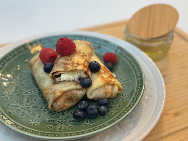 Golden-brown East-European Blini (stuffed crepes) filled with sweet Twarog cheese, served with fresh raspberries, blueberries, and honey. A delicious and authentic dessert, perfect for breakfast or a sweet snack.