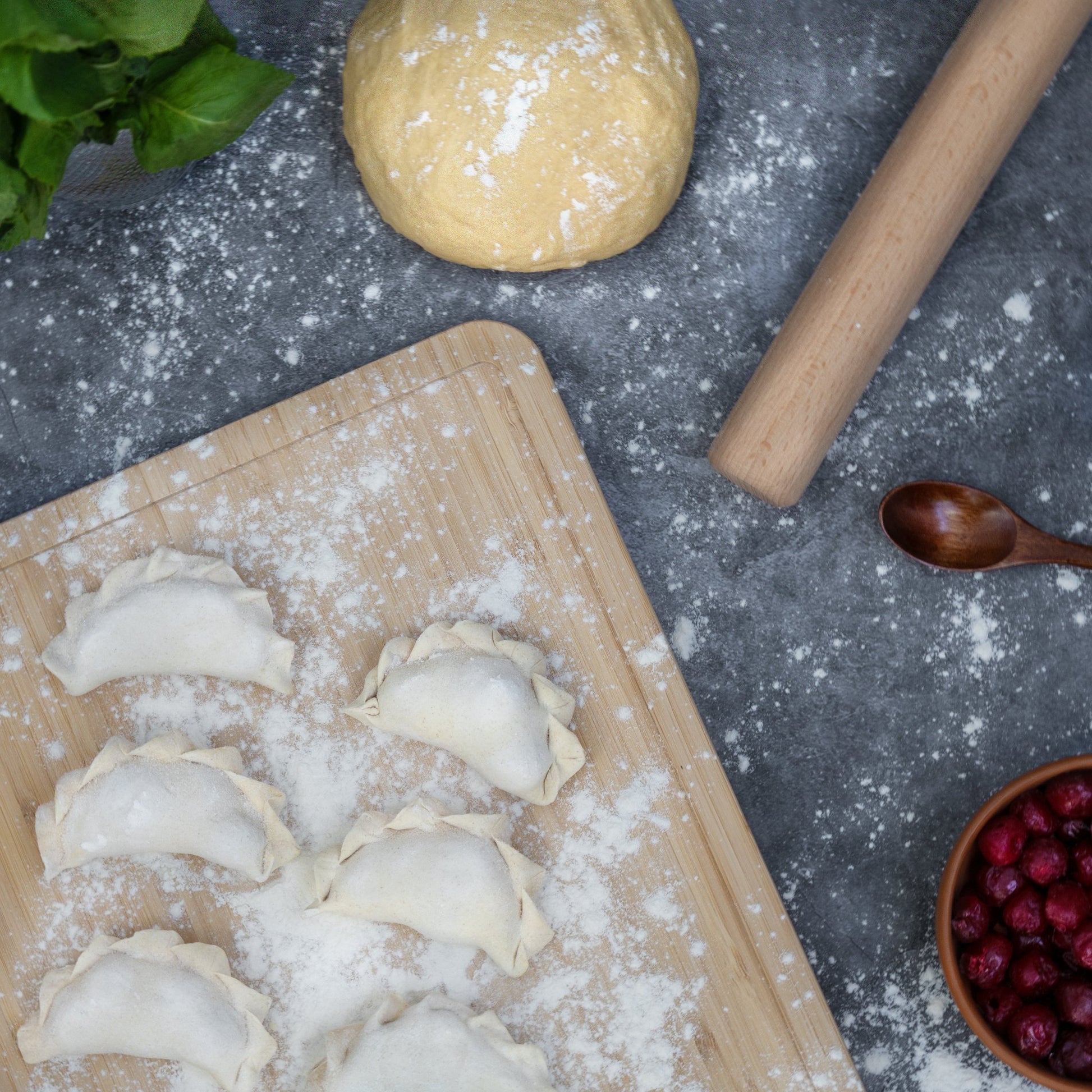 Uncooked sour cherry varenyky on floured board with dough and rolling pin—traditional dessert dumpling prep.