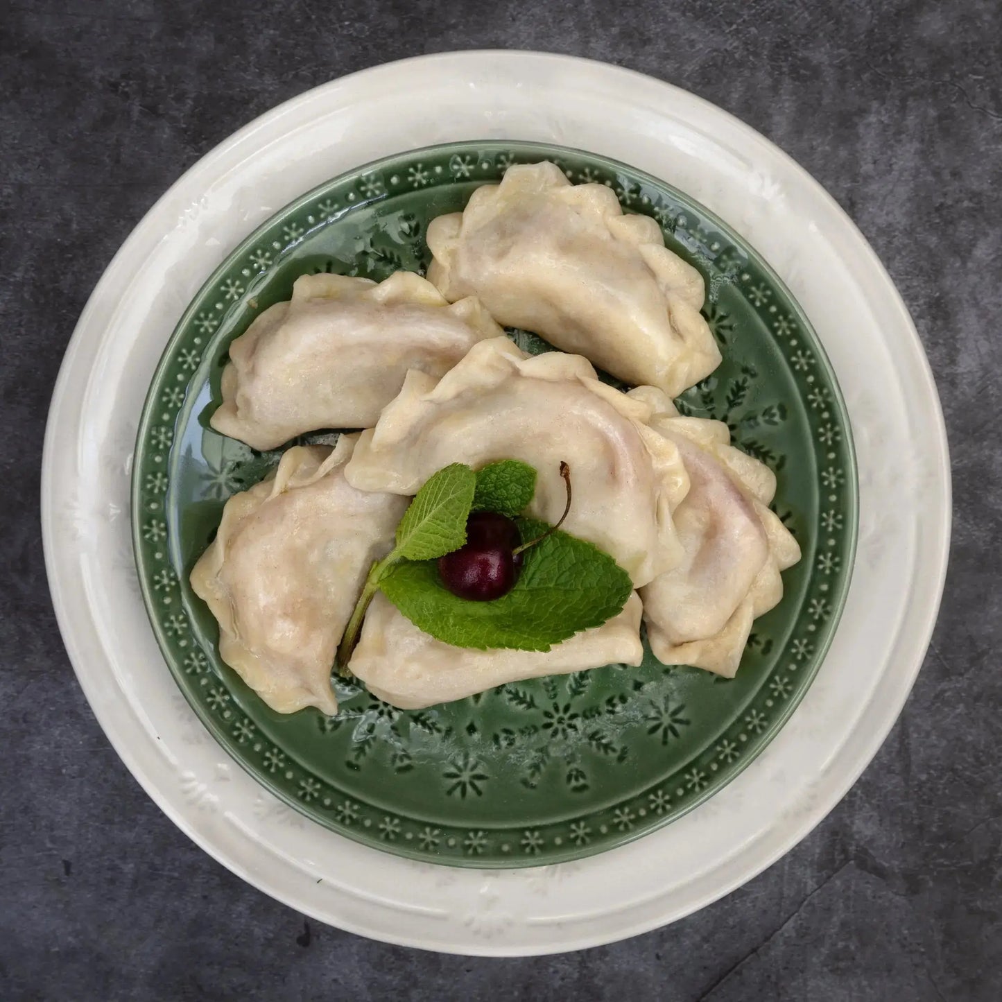 Top view of sour cherry varenyky with mint and cherry garnish—authentic Slavic dessert dumplings.