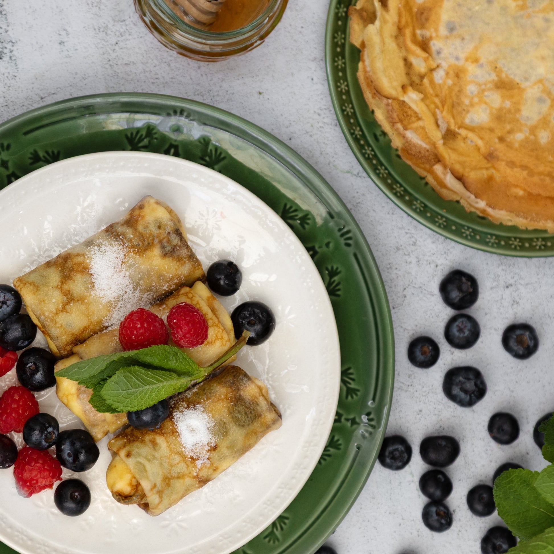 Top view of twarog crepes with raspberries, blueberries, and mint—sweet Eastern European rolled pancakes.