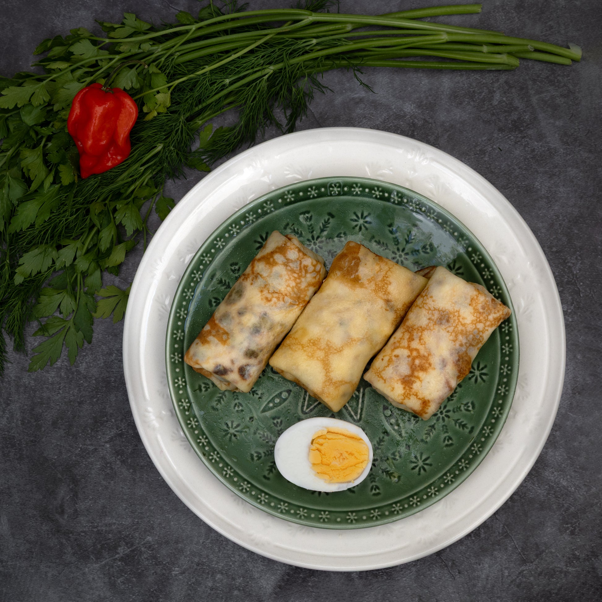 Cooked Eastern European-style chicken crepes on a green plate, served with hard-boiled egg and fresh herbs – Rassoul ready-to-eat meal.