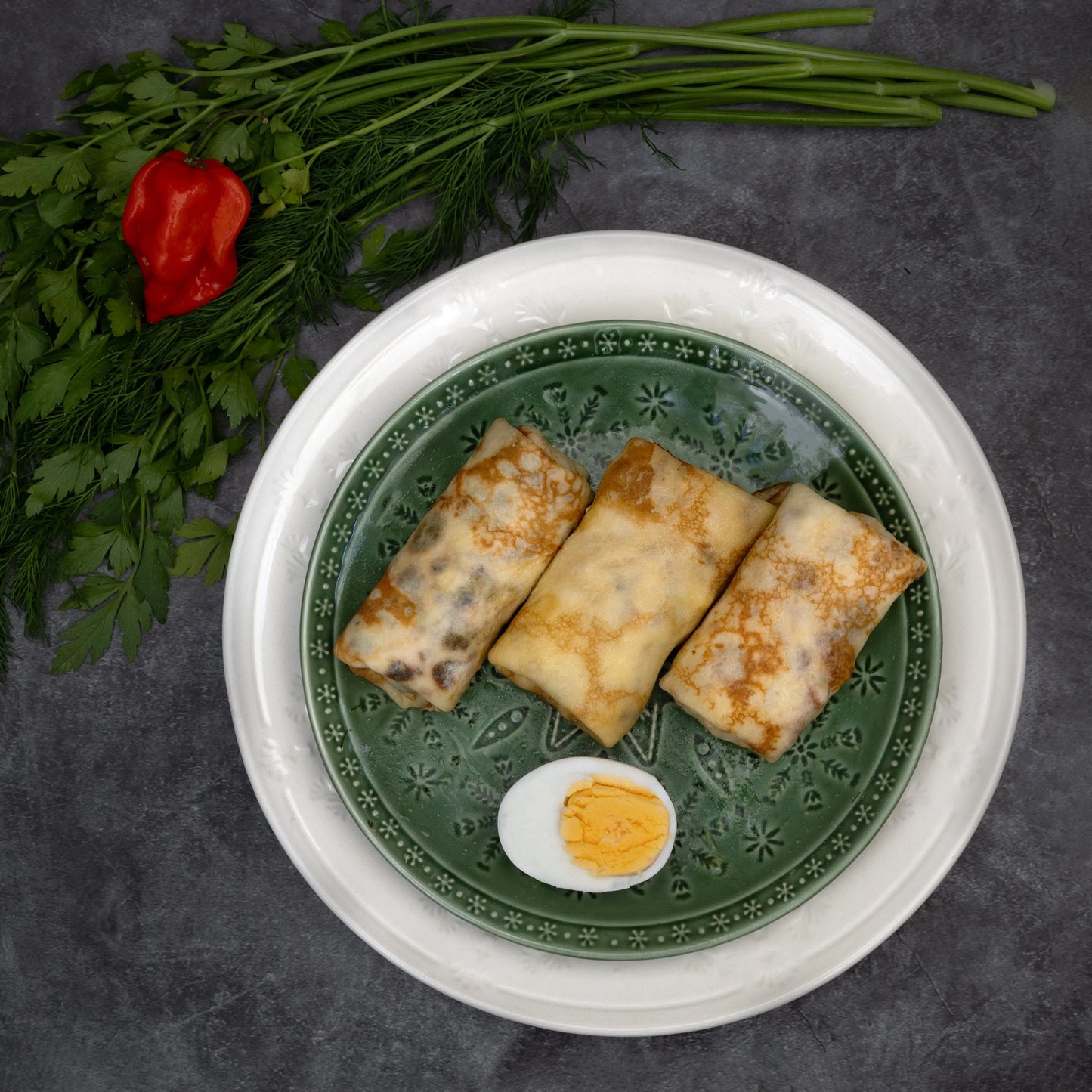 Cooked Eastern European-style chicken crepes on a green plate, served with hard-boiled egg and fresh herbs – Rassoul ready-to-eat meal.