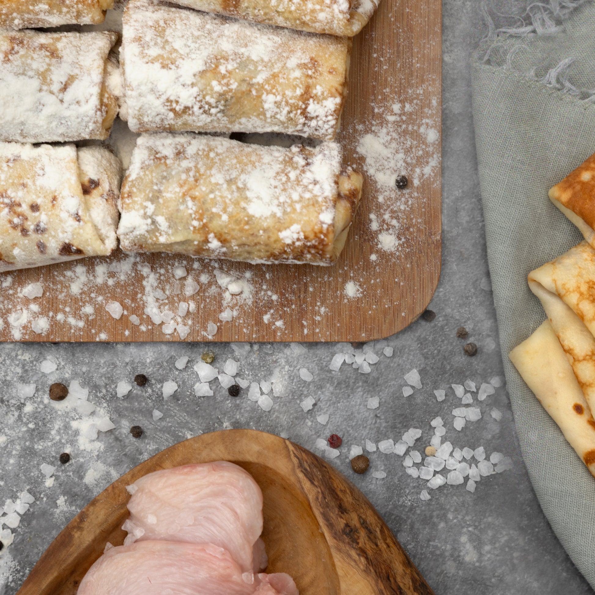Frozen chicken crepes dusted with flour on a cutting board with cooked chicken breast and spices – traditional Eastern European food by Rassoul.