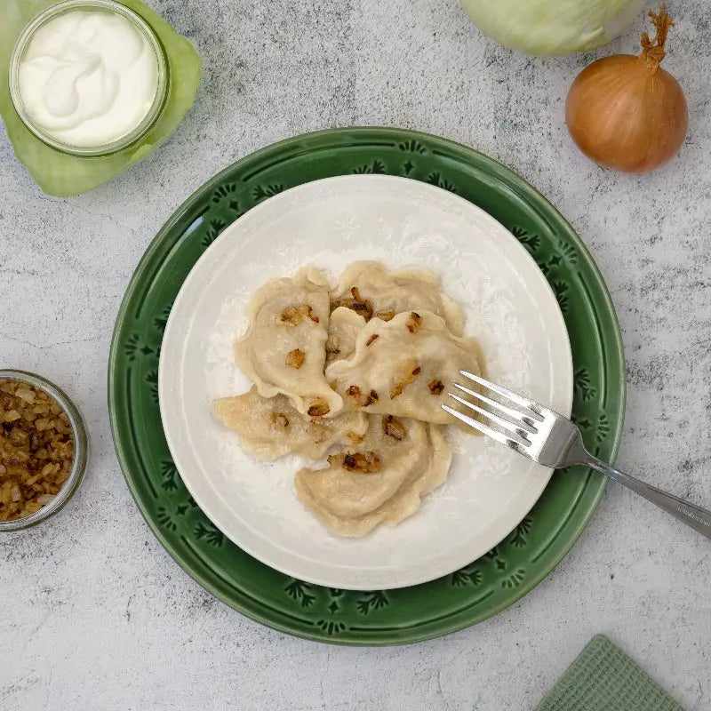 Cooked cabbage varenyky dumplings served on a plate with fried onions and sour cream – traditional Eastern European dish by Rassoul.