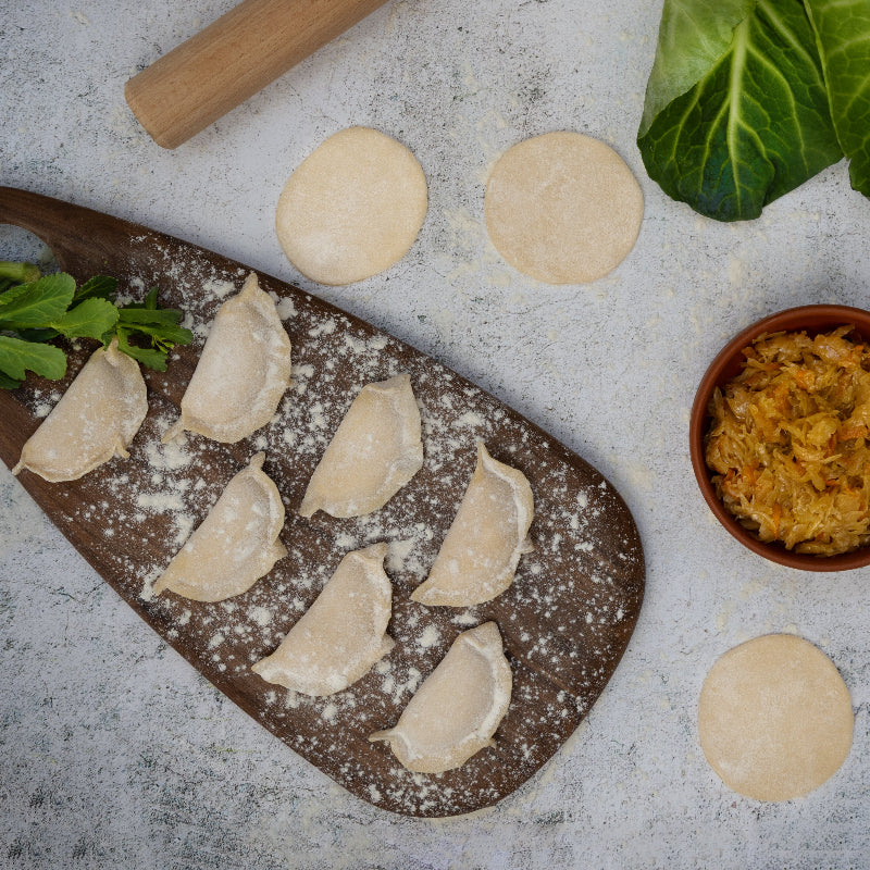 Uncooked cabbage varenyky dumplings on a floured board with fresh cabbage filling – handmade Eastern European dumplings from Rassoul