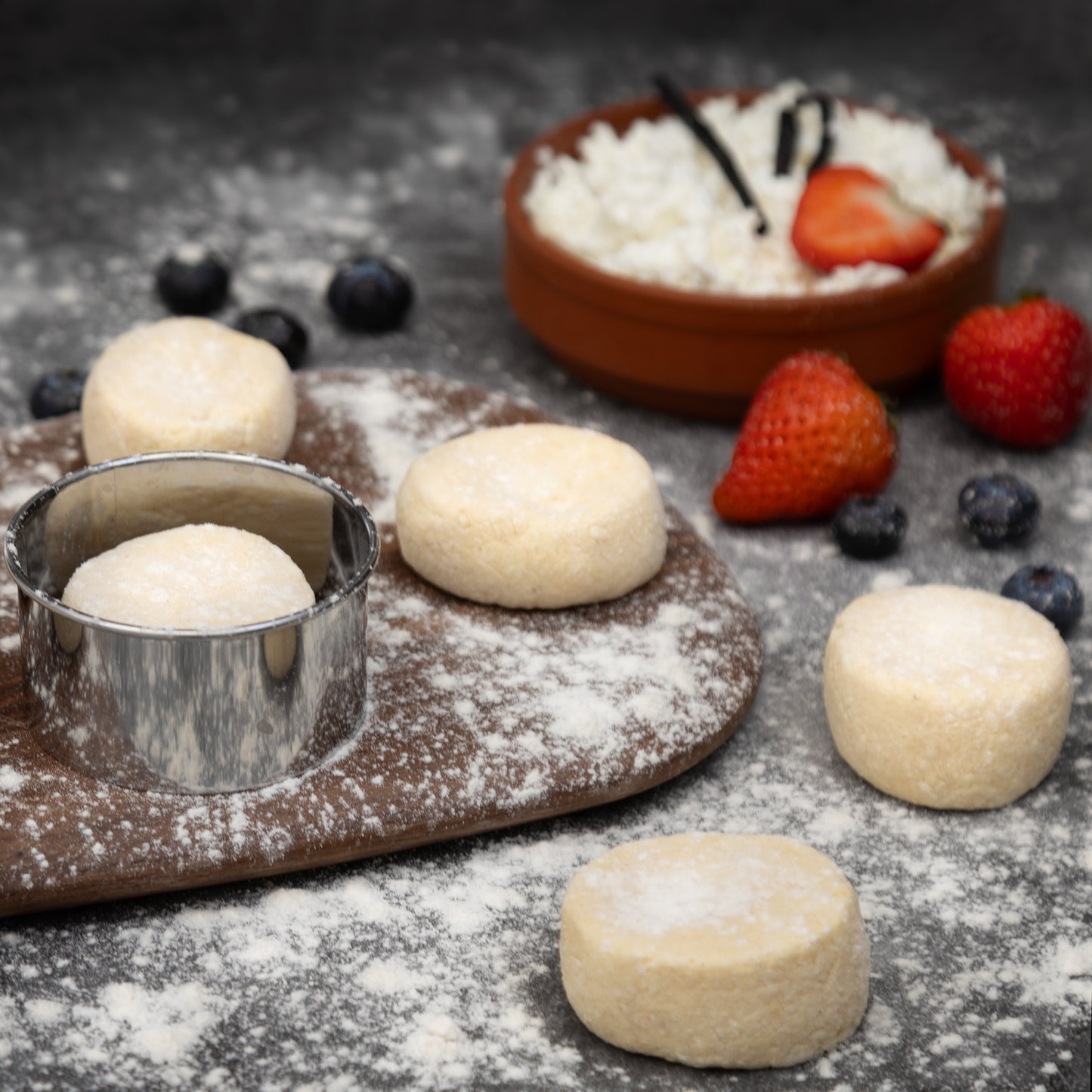 Raw Syrnyky dough rounds on floured board with cottage cheese, vanilla, and berries – authentic Eastern European pancakes prepared by Rassoul.