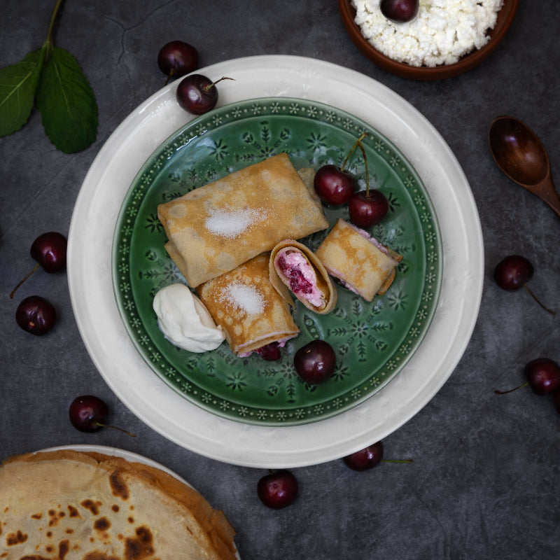 Authentic Eastern European crepes filled with twarog cheese and sour cherries, served with sour cream on a green plate by Rassoul.