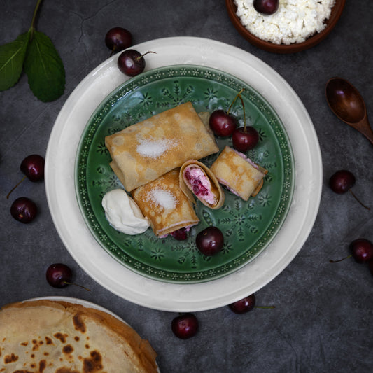 Authentic Eastern European crepes filled with twarog cheese and sour cherries, served with sour cream on a green plate by Rassoul.